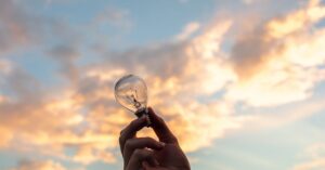 A hand holds a light bulb against a scenic sunset sky, symbolizing creativity and innovation.