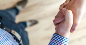 Close-up of a handshake between two people inside an office, symbolizing trust and cooperation.